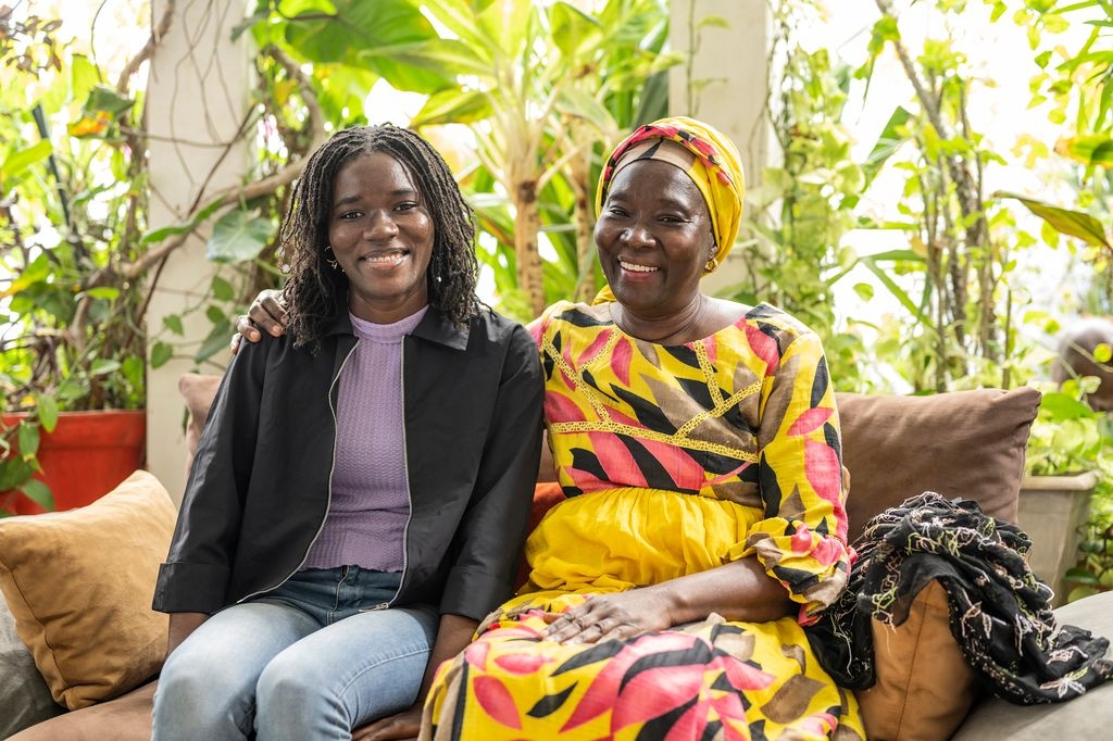 Silberia Diack og moren hennes sitter på en sofa i et godt opplyst rom. De holder hverandre i hendene og smiler.