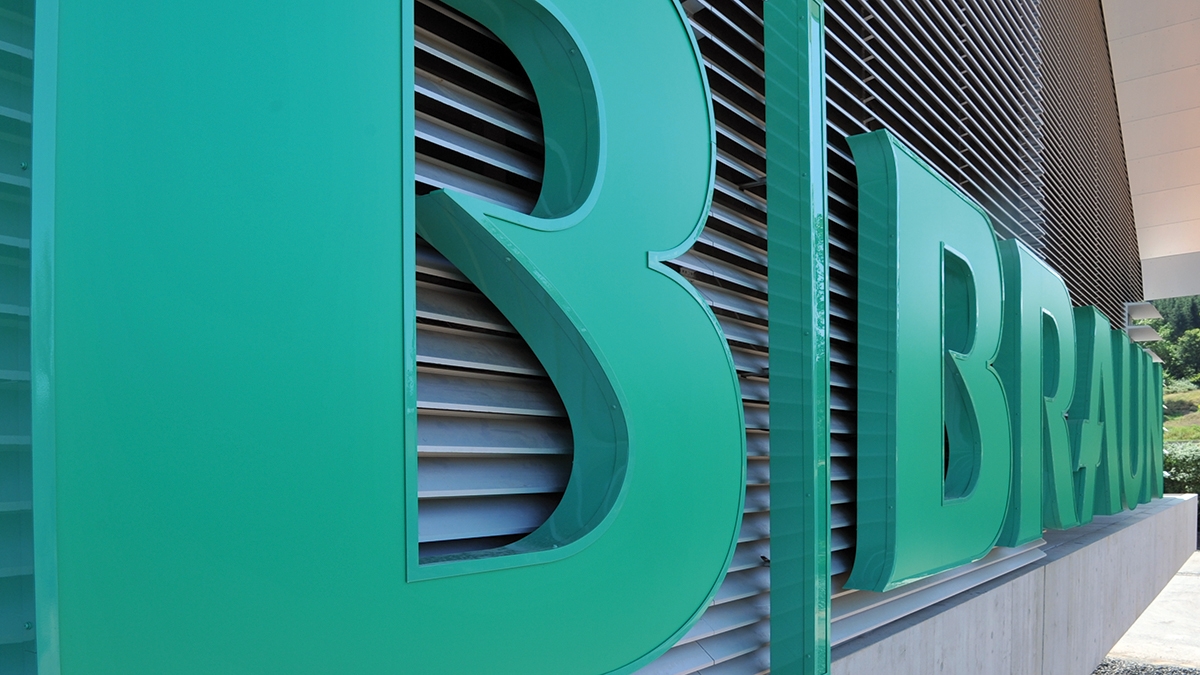 Nærbilde av et tredimensjonalt B. Braun-logo på fasaden av en moderne bygning.