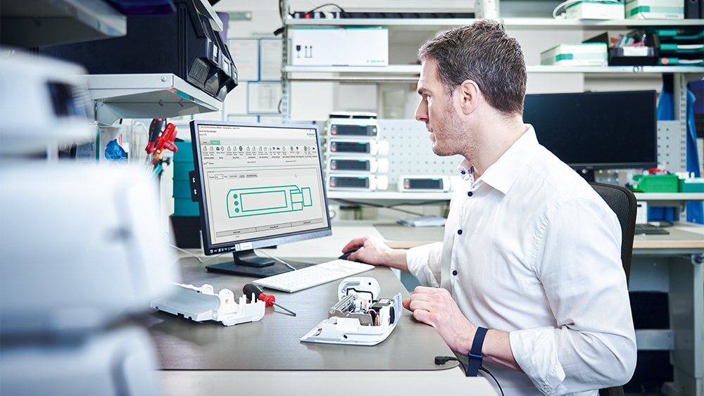 Biomed sitter foran datamaskinen og reparerer en infusjonspumpe