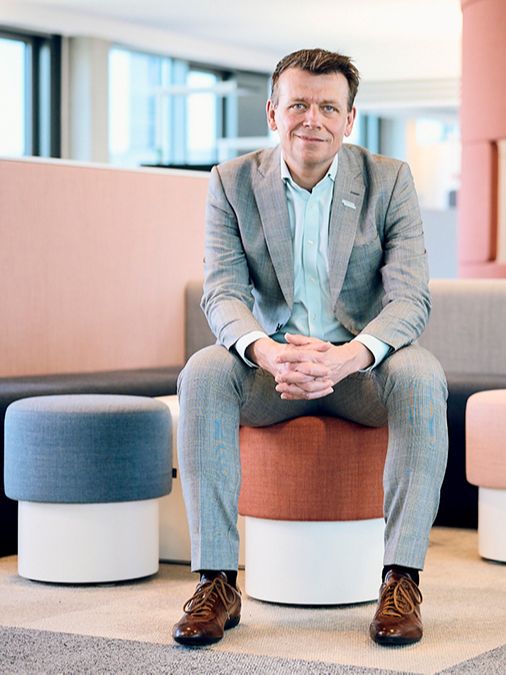 Dr. Michael Lauk sitter på en rød stoffkrakk i et moderne kontor, smiler og har hendene foldet. 